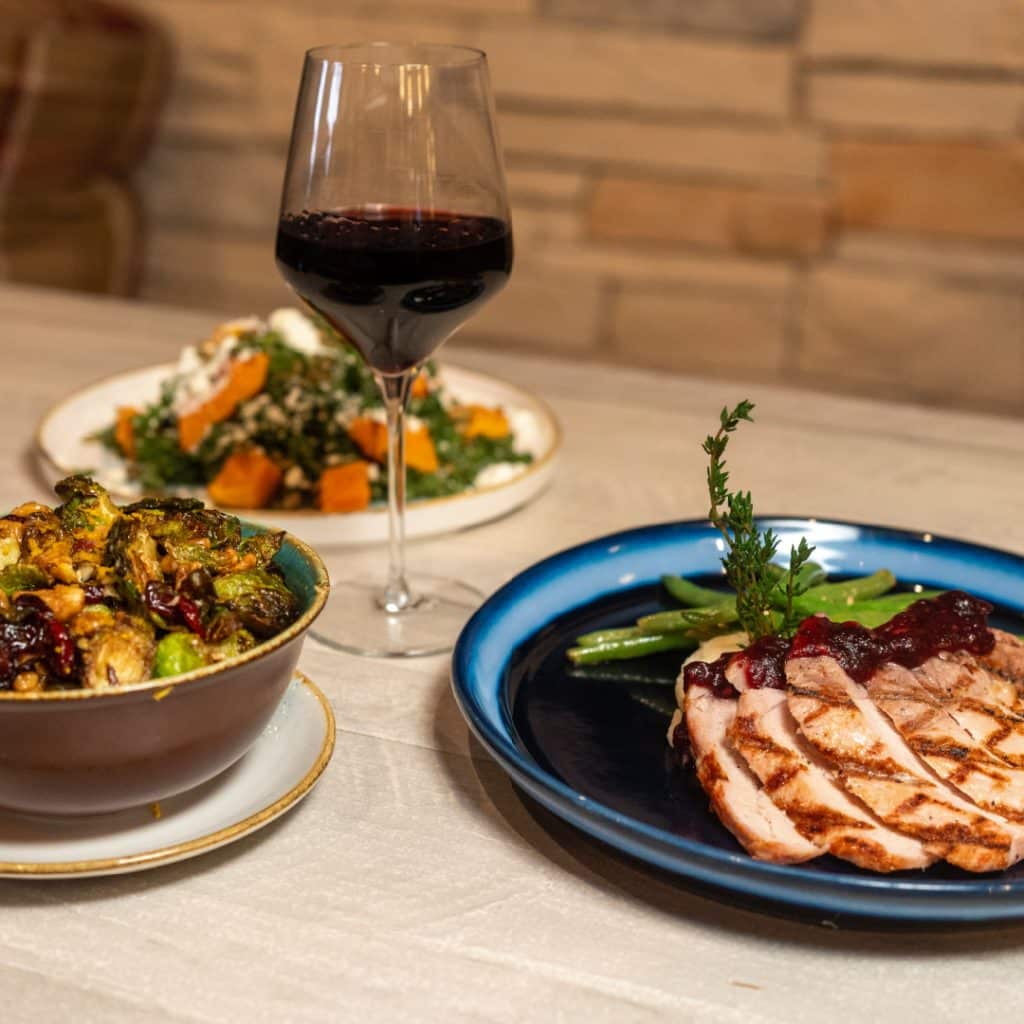 Sliced grilled chicken with cranberry glaze and green beans on a blue plate, garnished with thyme.