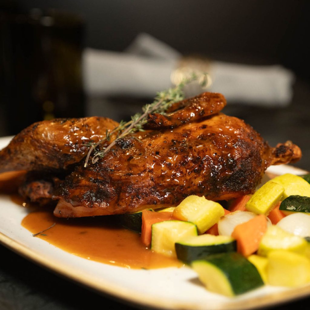 Roasted chicken with glaze on plate, garnished with a sprig of thyme and a side of mixed sautéed vegetables (zucchini, squash, carrots, onions).